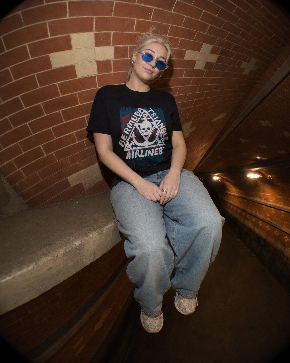Model wearing the Rough Draft Bermuda Triangle Airlines hand-screened graphic t-shirt in a brick tunnel, close lifestyle photo.
