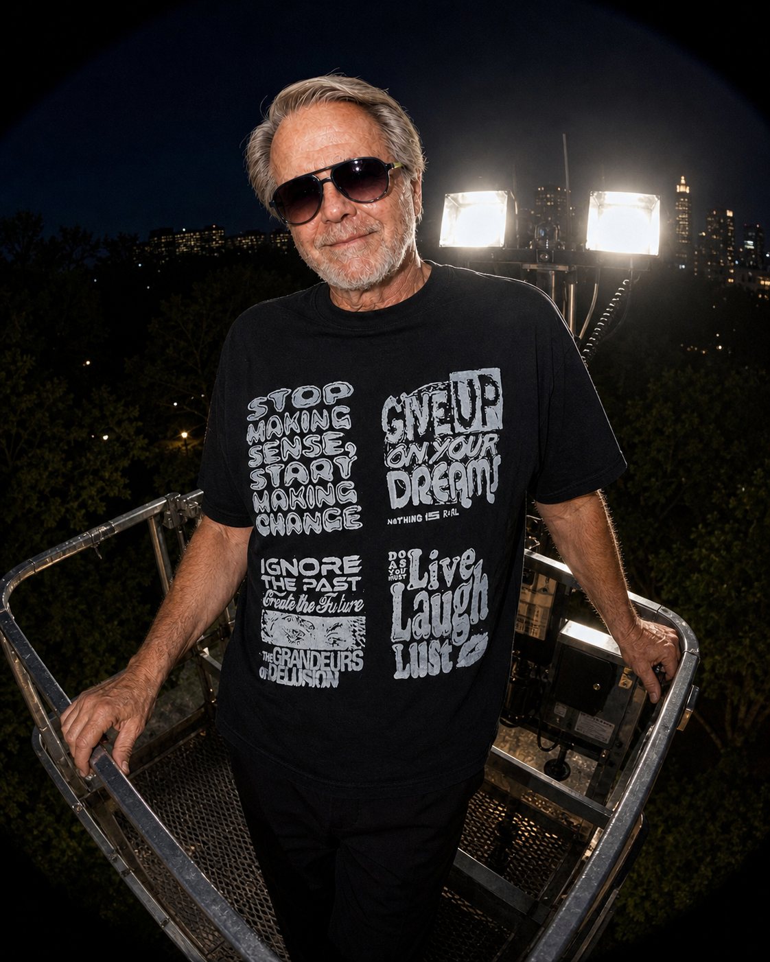 Model wearing the Rough Draft Stop Making Sense Medley hand-screened graphic t-shirt on a light tower at night, close lifestyle photo.
